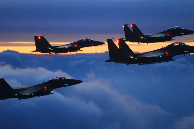 Four F-15Ks silhouetted above a cloud layer at dusk with navigation lights lit