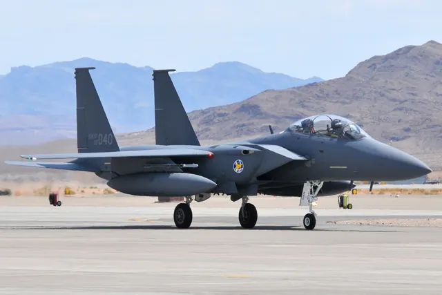 An F-15K taxiing at a desert airfield with bare mountains in the background
