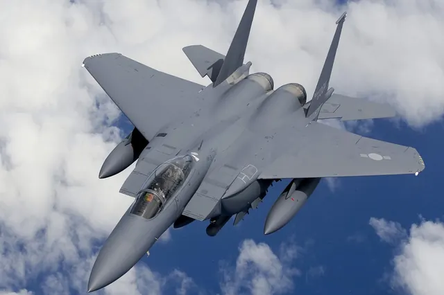 An F-15K climbing and banking against blue sky and scattered cloud