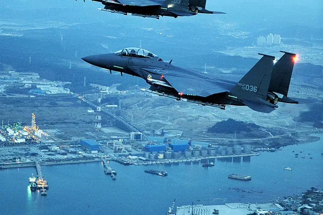 Four F-15Ks flying over a coastal industrial port at dusk