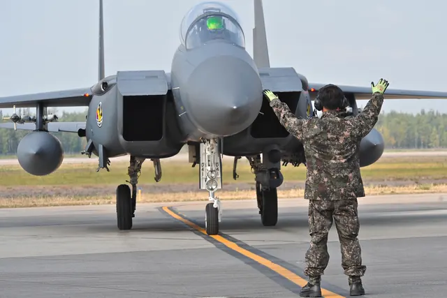 A ground crewman in camouflage marshalling an F-15K taxiing towards him