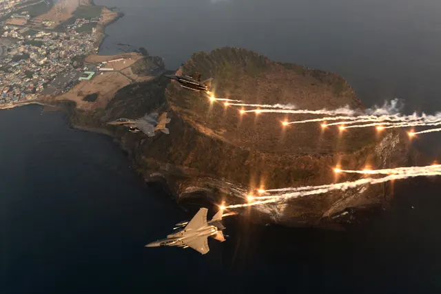 Three F-15Ks dispensing decoy flares as they pass over a coastal crater headland