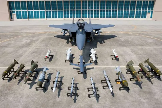 An F-15K parked in front of a hangar with rows of missiles and bombs on ground stands