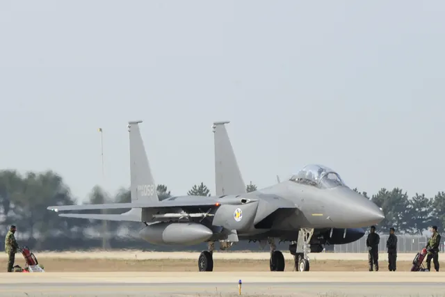 An F-15K on the ramp with ground crew and wheeled fire extinguishers nearby