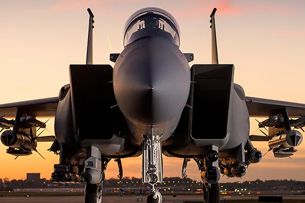 An F-15K parked nose-on at an airfield at sunset with missiles under both wings