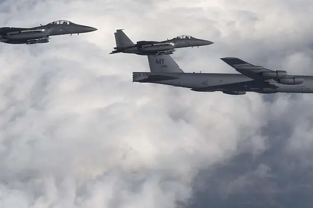 Two F-15Ks flying alongside a B-52 bomber above a cloud layer