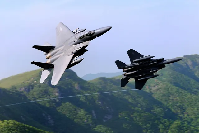 Two F-15Ks banking steeply in front of green forested mountains