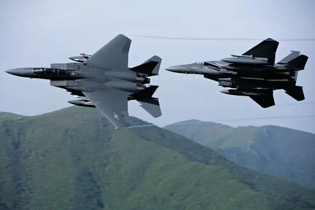 Two F-15Ks seen from above as they bank over green hills